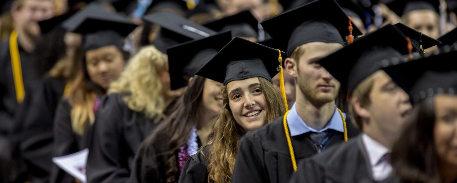 SPU graduates line up to begin the Commencement ceremony; one young graduate leans to her left, smiling, 朝舞台前面看.